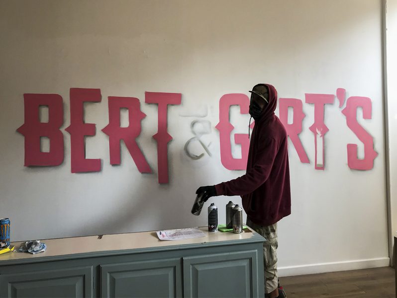 A man is painting an office branding sign for Bert & GT's.