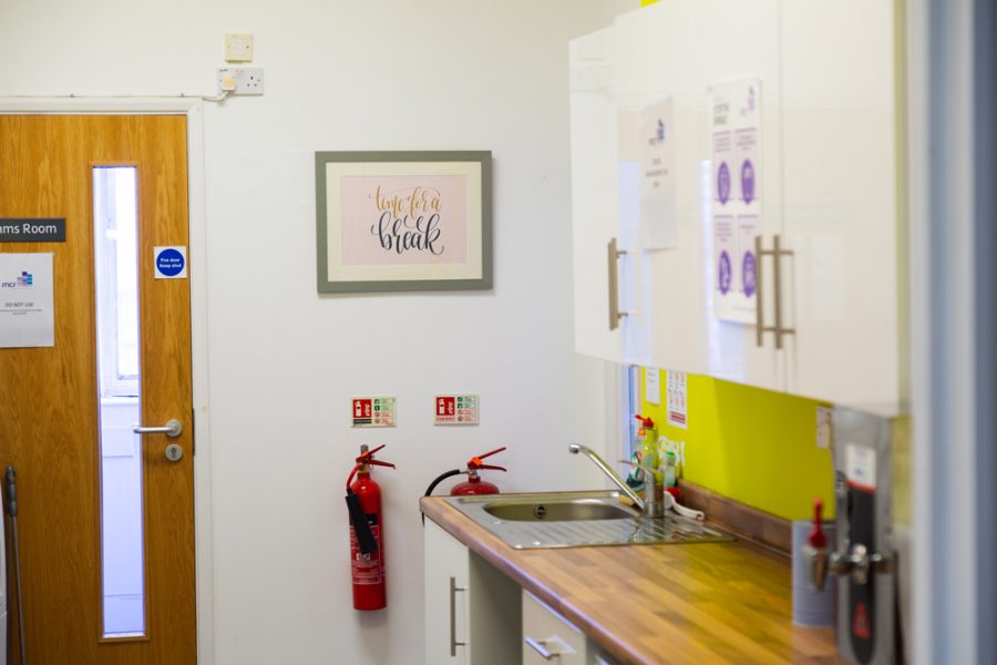 An office bathroom featuring a sink and a prominently displayed fire extinguisher, aligned with the company's branding.