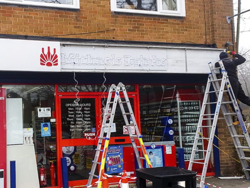 A man is working outside, installing office branding on a ladder outside of a store.